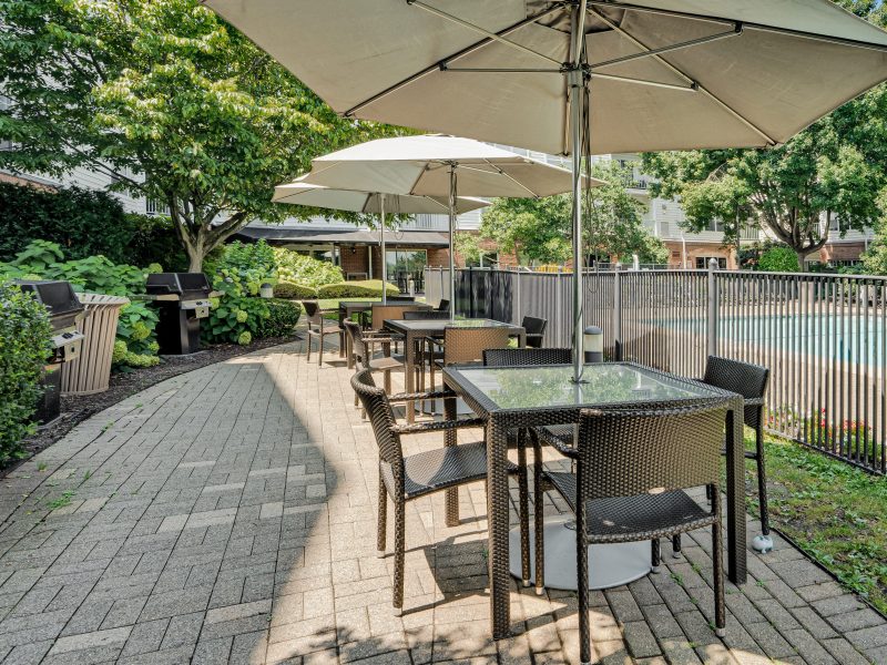 Outdoor dining and poolside lounge area at TGM Anchor Point with greenery and umbrellas.