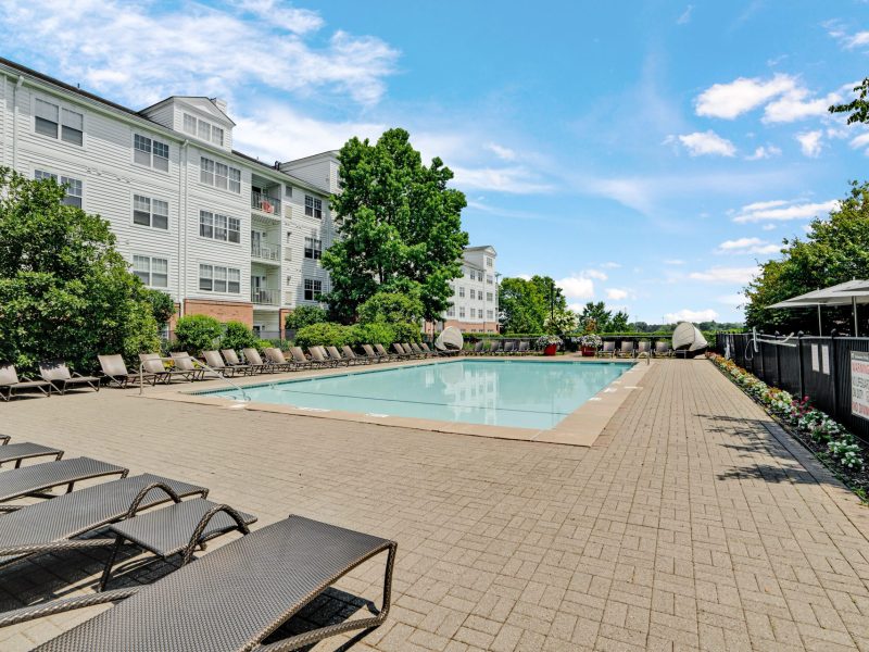 Modern apartment pool with lounge chairs, clear blue water, and sunny relaxing atmosphere.